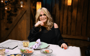 Laulaja istuu Vain elämää -pöydässä ja hymyilee kameralle. Kuva: 2025.