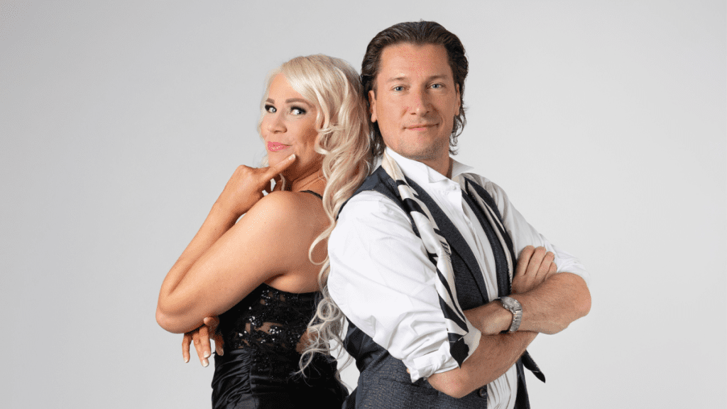 Kaksi juhlavaan esiintymisasuun pukeutunutta laulajaa seisoo selät vastakkain ja hymyilee kameralle.