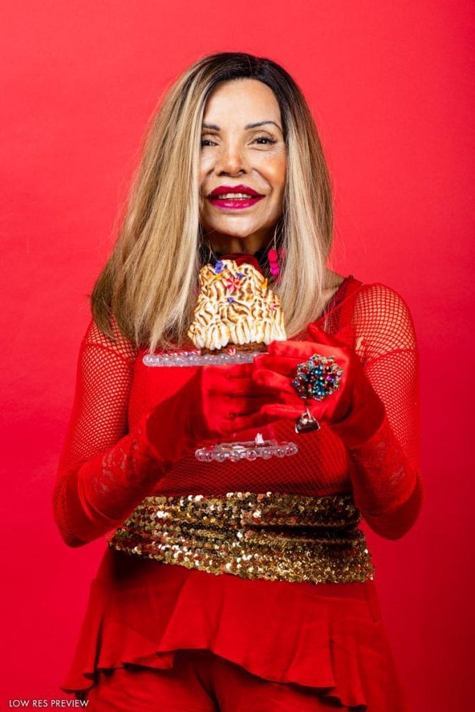 Studiokuva jossa nisa soraya poseeraa punaista taustaa vasten juhlallisessa punaisessa asussa ja pitää kakkua kädessään