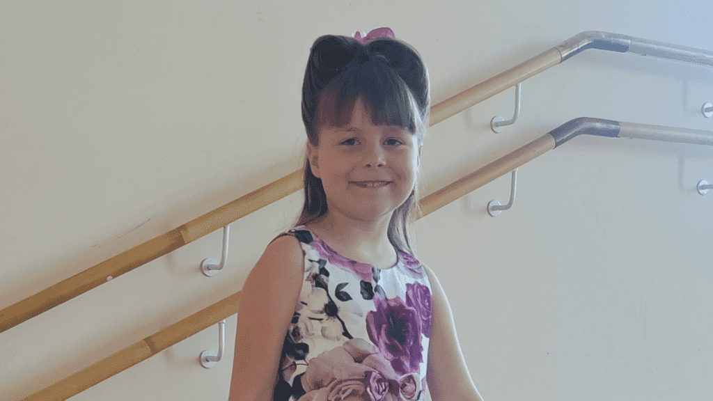 Sylvi Takatalo, 8, Suomen nuorin iskelmäartisti hymyilee juhlamekossa portaikon edessä.