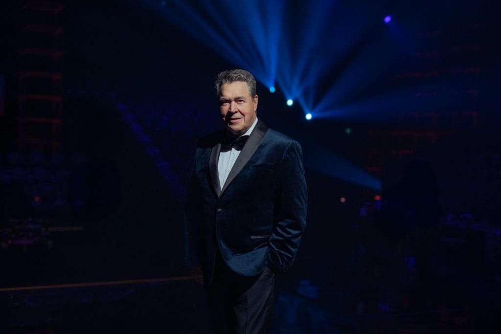Markku Aro tummassa esiintymispuvussa konserttisalin valojen keskellä, suomalainen iskelmälaulaja ja kevään 2026 kiertueen tähti.