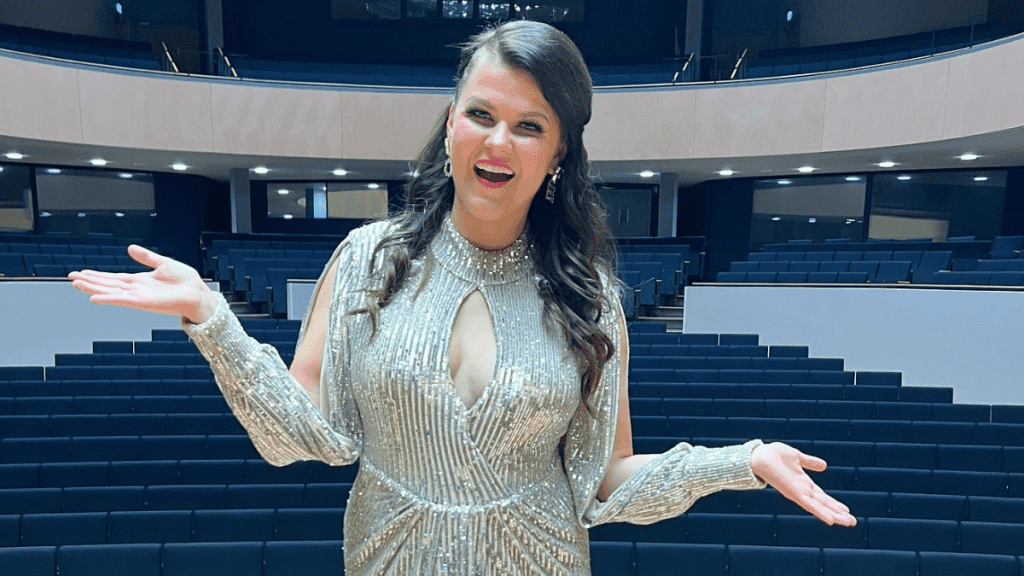 Laulaja Saara Aalto poseeraa kädet levällään hopeanhohtoisen ilapuku päällään konserttisalissa 2025