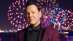 kari hirvonen poseeraa viininpunaisessa takissa, taustalla ilotulitusraketteja 2025