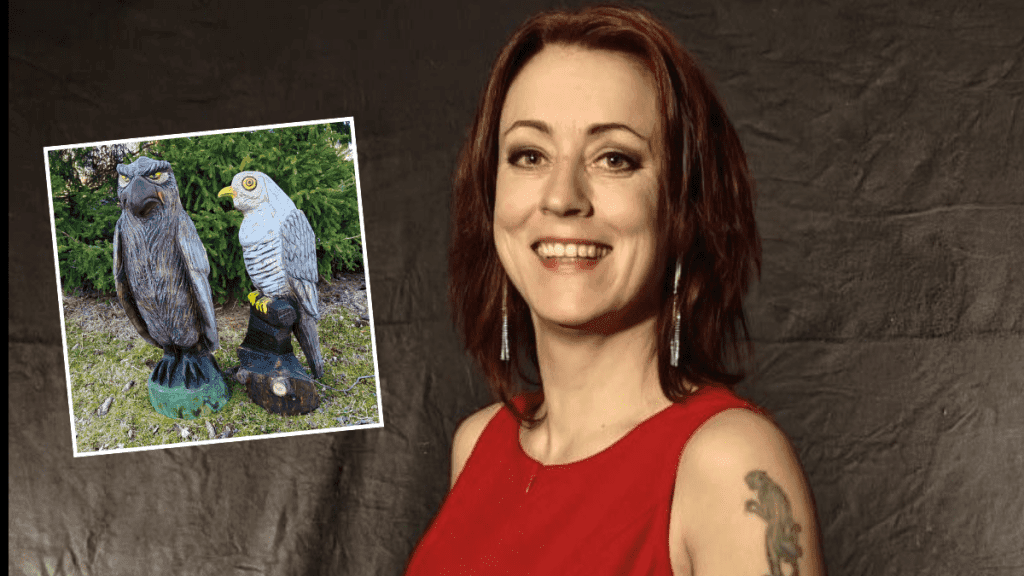Smiling woman in a red sleeveless top poses beside a tilted photo of two carved owl statues outdoors, one brown and one gray, on a green base and tree background.
